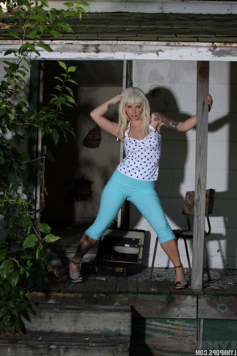 15P Die sexy Blondine mit Tätowierungen Lynn Pops zieht sich hinter einem verlassenen Haus aus