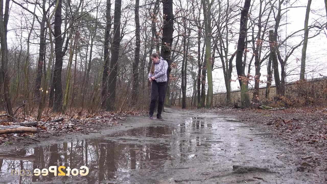 15P Mulher caucasiana abaixa as calças para fazer xixi em uma poça espalhada na estrada