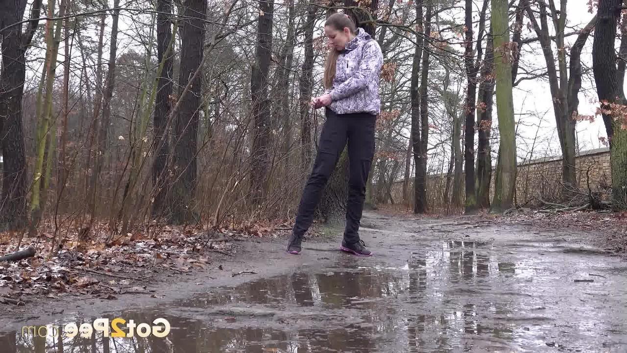 15P Mulher caucasiana abaixa as calças para fazer xixi em uma poça espalhada na estrada