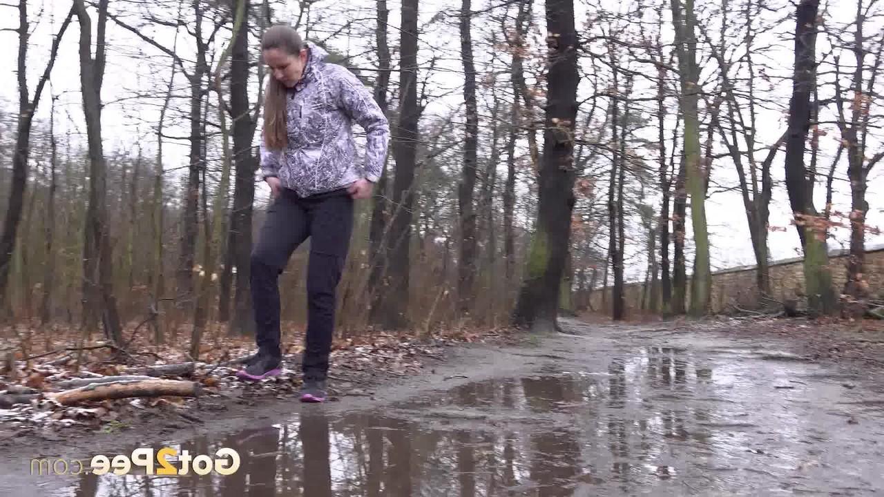 15P Mulher caucasiana abaixa as calças para fazer xixi em uma poça espalhada na estrada