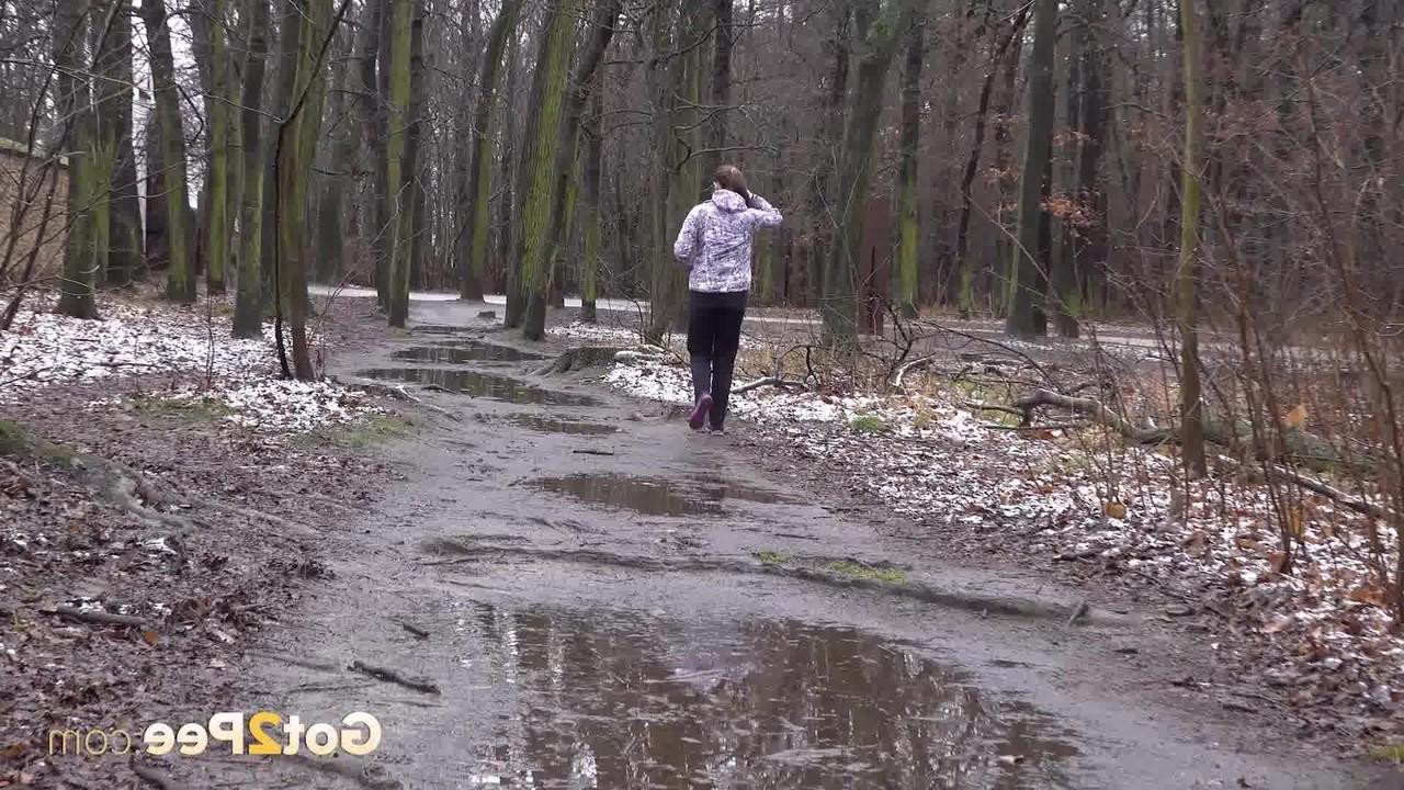 15P Mulher caucasiana abaixa as calças para fazer xixi em uma poça espalhada na estrada