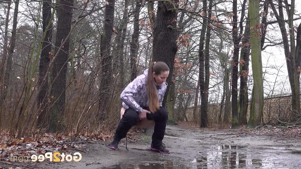 15P Mulher caucasiana abaixa as calças para fazer xixi em uma poça espalhada na estrada