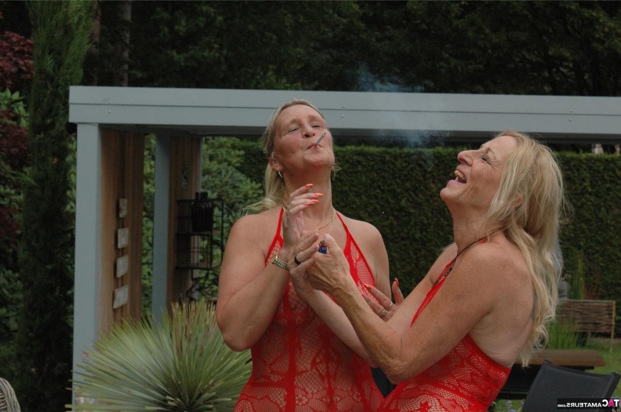 16P Two older blondes in red lingerie smoke while teasing an old man in a garden