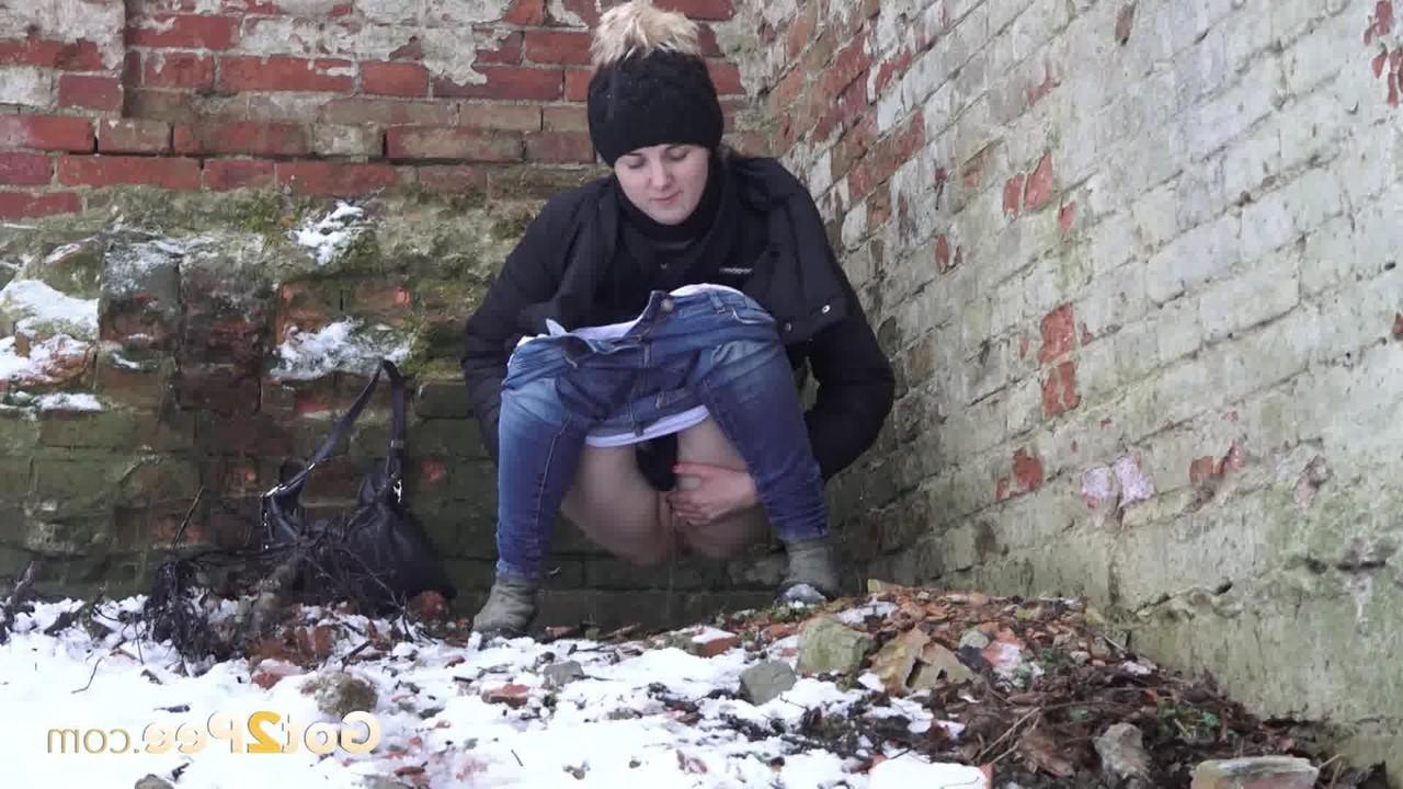 15P A garota branca Katya faz xixi no chão coberto de neve contra um prédio de tijolos
