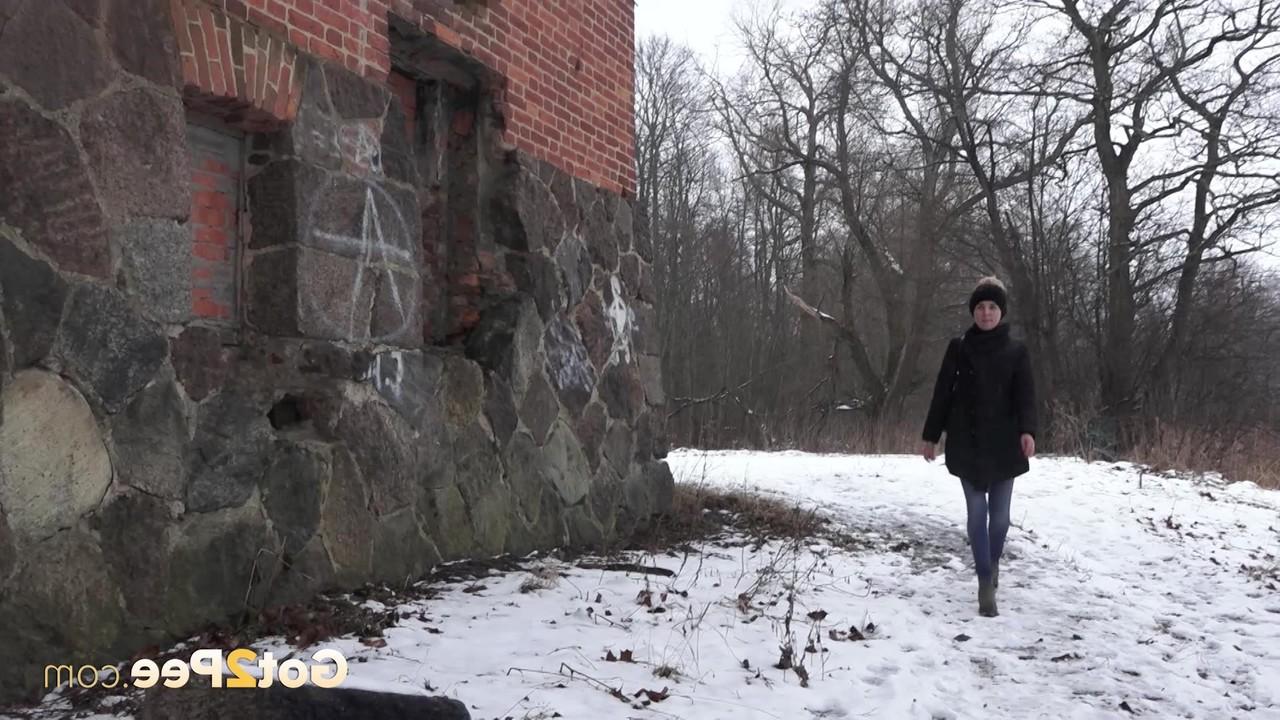 15P A garota branca Katya faz xixi no chão coberto de neve contra um prédio de tijolos