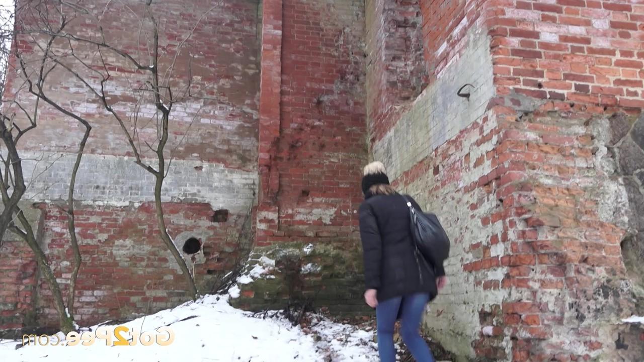 15P A garota branca Katya faz xixi no chão coberto de neve contra um prédio de tijolos