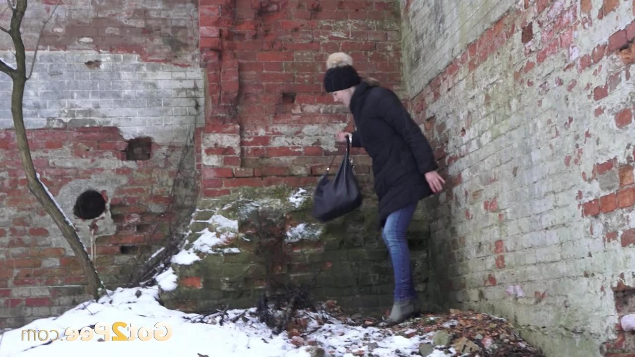 15P A garota branca Katya faz xixi no chão coberto de neve contra um prédio de tijolos