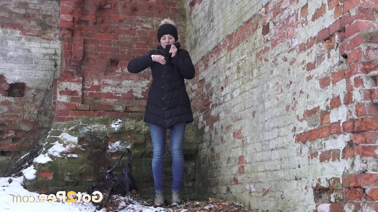 15P A garota branca Katya faz xixi no chão coberto de neve contra um prédio de tijolos