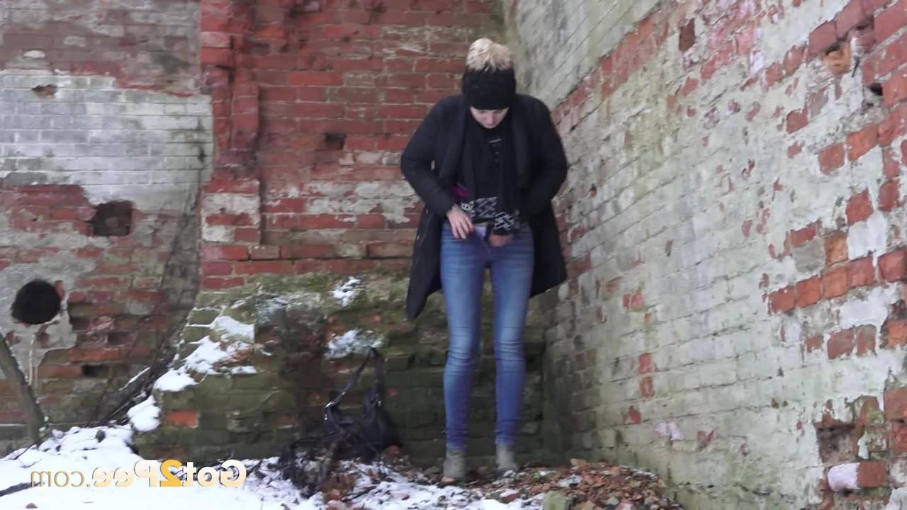 15P A garota branca Katya faz xixi no chão coberto de neve contra um prédio de tijolos