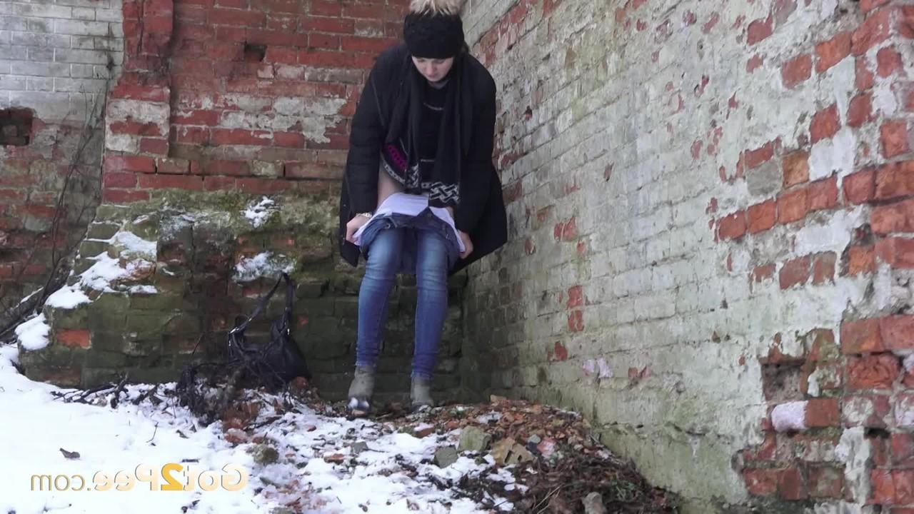 15P A garota branca Katya faz xixi no chão coberto de neve contra um prédio de tijolos