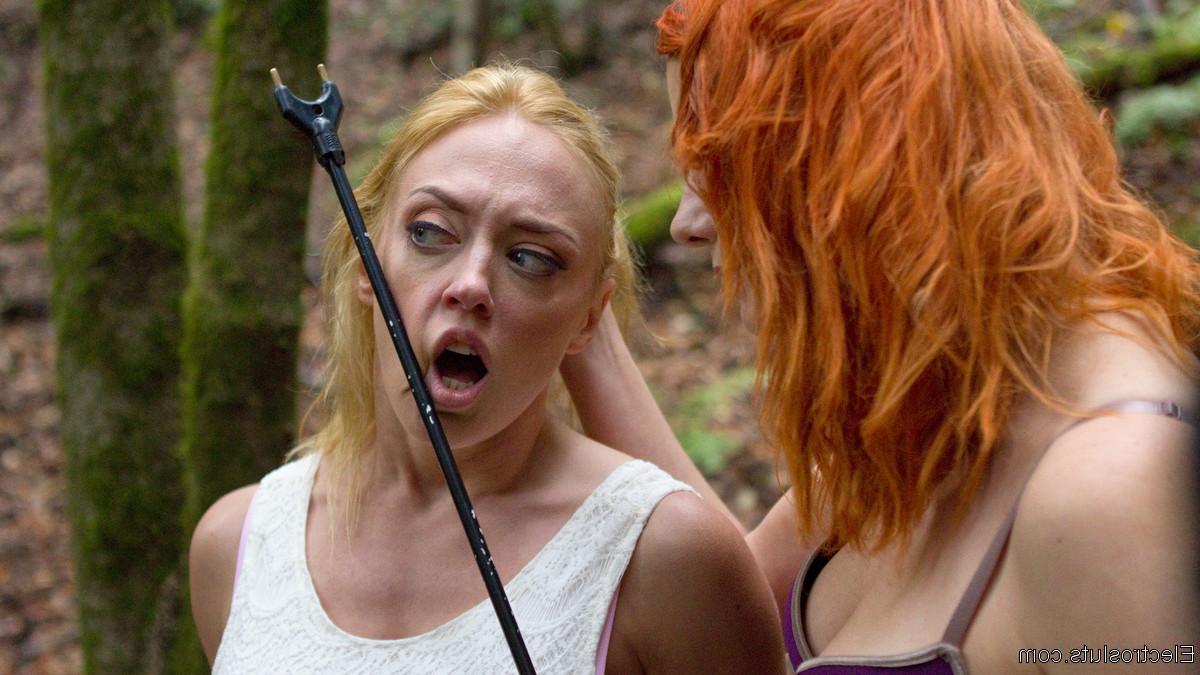 15P Une dominatrice rousse soumet la fille blonde Dee Williams à un aiguillon pour le bétail dans les bois.