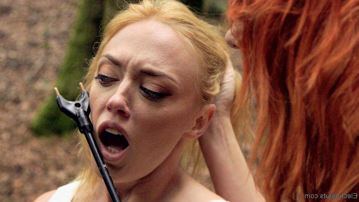 15P Une dominatrice rousse soumet la fille blonde Dee Williams à un aiguillon pour le bétail dans les bois.