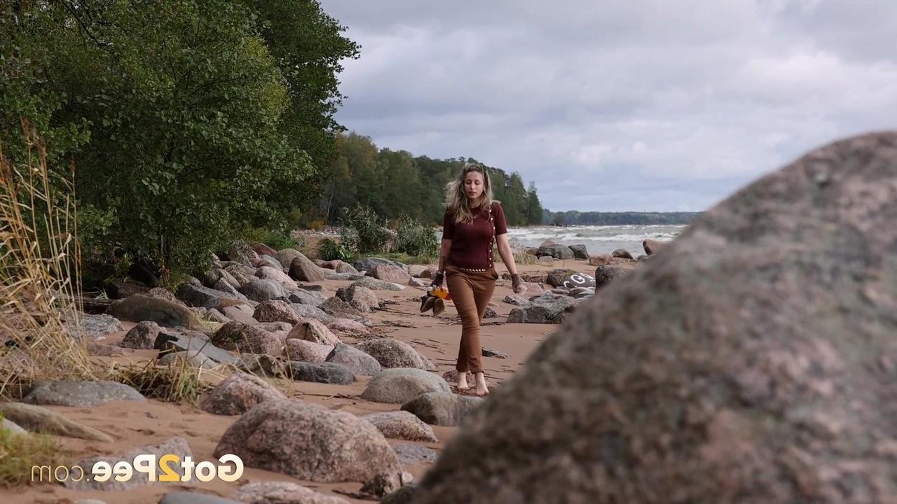 15P Katy Dee leans back against a boulder on a beach for a badly needed piss