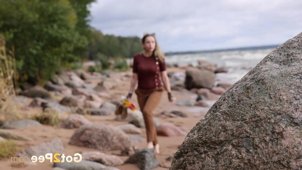 15P Katy Dee leans back against a boulder on a beach for a badly needed piss