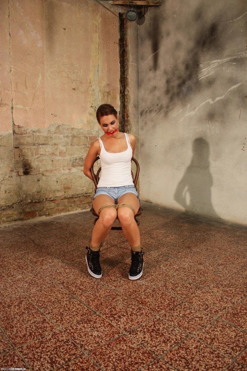 20P Wunderschöne Brünette posiert in Jeansshorts und einem weißen Tanktop an einen Stuhl gefesselt