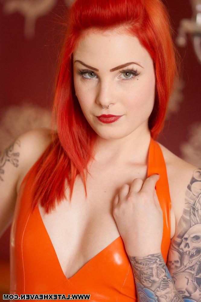12P Sexy redhead with tattoos models a latex dress and stockings in a bedroom