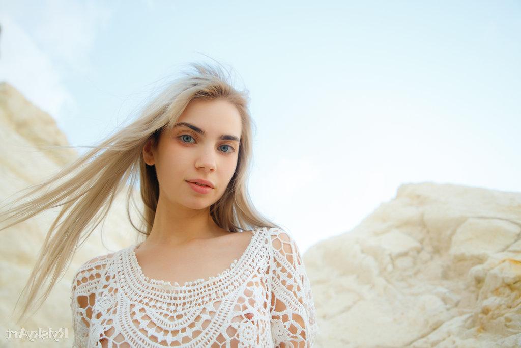 16P Sofy Bee, une jeune blonde platine, enlève sa robe en dentelle pour se mettre nue sur un sol rocailleux.