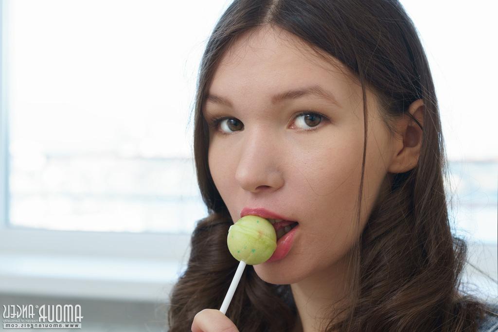 20P Young beauty Ariel licks a sucker while getting totally naked on a bed
