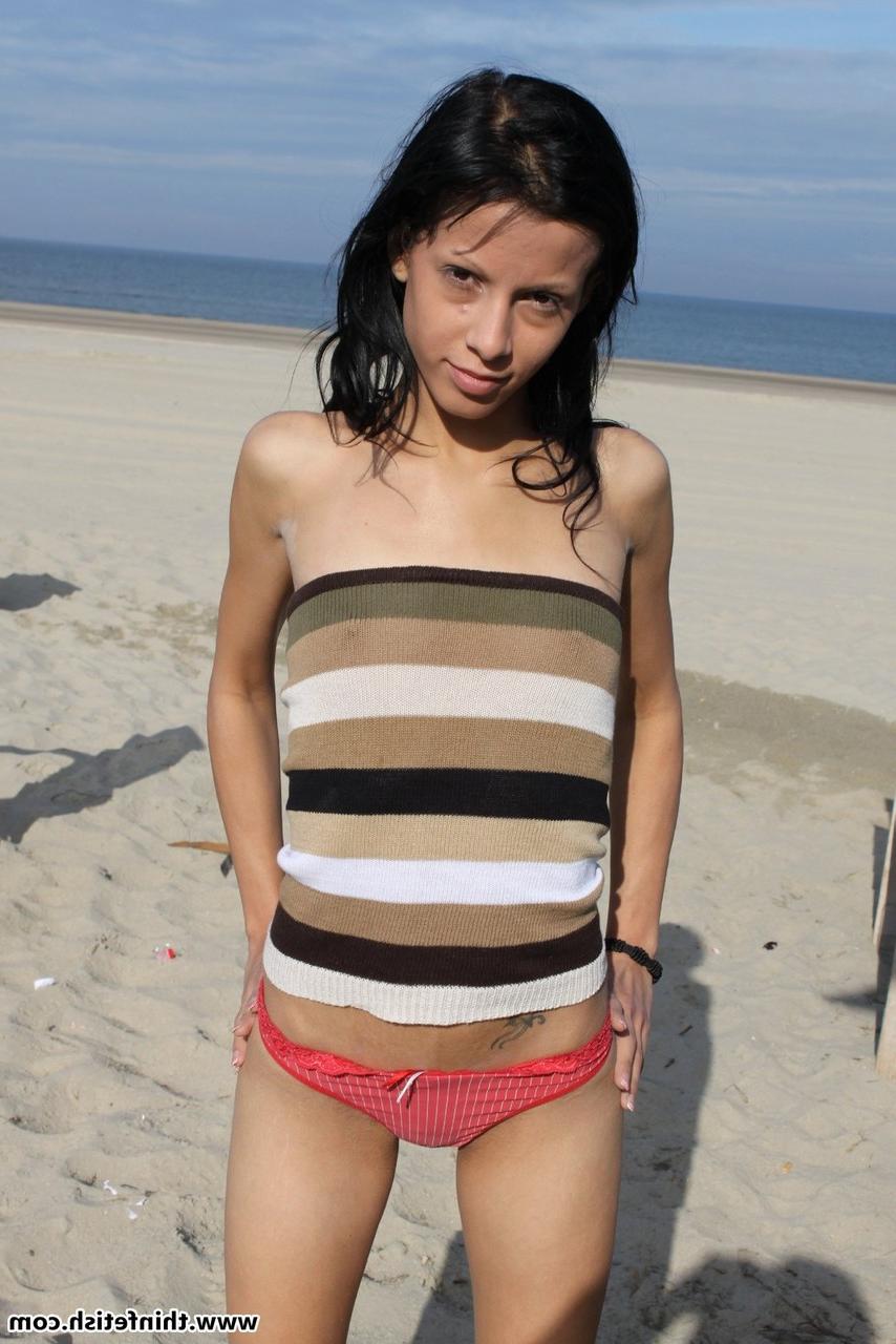 16P Une brune mince tient son cul nu pieds nus sur une plage de sable